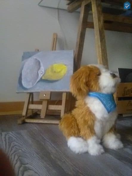 Stuffed animal in front of easel with painting of lemon and beach shell.